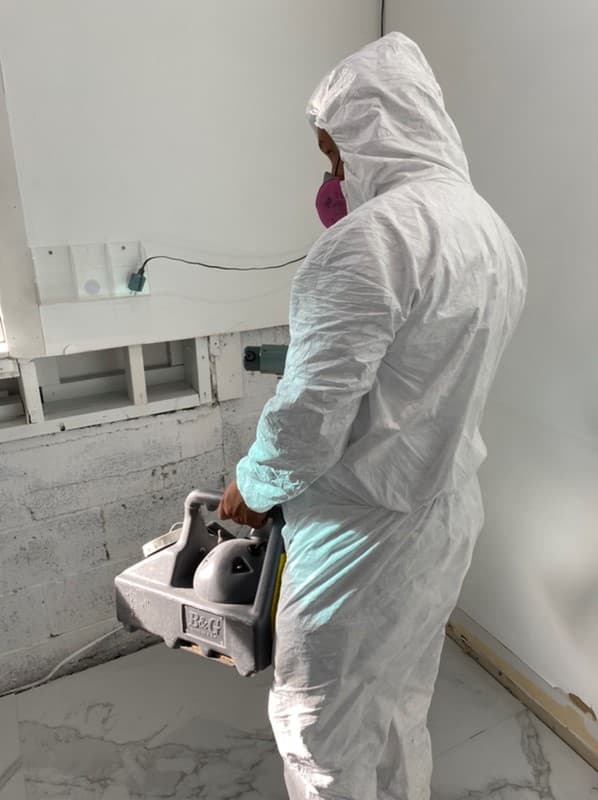 Swift Restoration technician in a protective suit treating a water-damaged wall after extraction